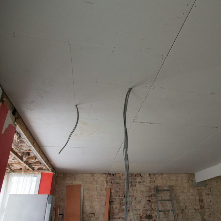 Decke mit Rissen und freiliegenden Kabeln, daneben ein Holzleiter.